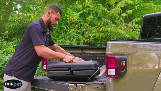 Video of man setting up a Mirapet foldable travel dog crate in the back of a pickup truck. When it's set up, a dog jumps inside and the man drives the dog away.